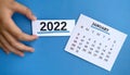 White January 2022 calendar with hand holding small white card of 2022. New Year Concept