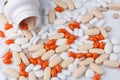 White jar with different pills spilling out on white background. Spilled orange and white pills