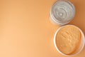 In a White jar, peach-colored body cream and scrub. Orange background.