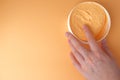 In a White jar, peach-colored body cream, woman's hand takes cream. Orange background. Copy space