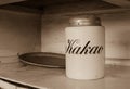 A white jar for storage cocoa with text `Kakao` in russian languige and an old metal tray with rust. Old white kitchen shelf. Sep
