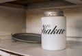 A white jar for storage cocoa with text `Kakao` in russian languige and an old metal tray with rust. Old white kitchen shelf. Age