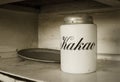 A white jar for storage cocoa with text `Kakao` in russian languige and an old metal tray with rust. Old white kitchen shelf.