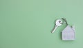 White key with a keychain in the form of a house on a light green background. The concept of buying, selling, renting real estate