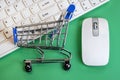 White keyboard and mouse for a computer on a green background. Shopping trolley lies on the keys. Concept online shopping, black Royalty Free Stock Photo