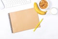 White keyboard, mouse, scetchbook; yellow pencils, plate with granola, banana and glass of milk on white background. Bright mockup Royalty Free Stock Photo