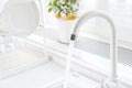 White kitchen faucet running with blurred windowsill and dish dryer