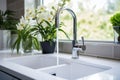 White kitchen faucet with a white sink and green plants in a stylish modern kitchen
