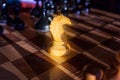 White knight staying against full set of black chess pieces. Closeup of chessboard with wooden pieces on table in sunlight, game Royalty Free Stock Photo