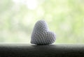 A white knitted heart lies on a gray area on a nature white and green background