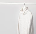 White knitted wool sweater on a white wooden hanger against the background of the light wall. Autumn and winter clothes. Store con