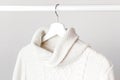 White knitted wool sweater on a white wooden hanger against the background of the light wall. Autumn and winter clothes. Store con