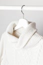 White knitted wool sweater on a white wooden hanger against the background of the light wall. Autumn and winter clothes. Store con