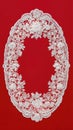 A white lace oval doily frame, top view, on a red background. The lace is embroidered with symmetrical openwork and an ornamental Royalty Free Stock Photo