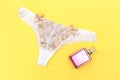 white lace pantie with beige knot and decorated with pink perfume bottle on yellow background.