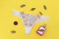 White lace pantie with beige knot and decorated with pink perfume bottle on yellow background. Royalty Free Stock Photo