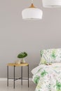 White lamp above leaf in vase on wooden bedside table in scandinavian bedroom, copy space on the empty grey wall Royalty Free Stock Photo