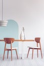 Lamp above long wooden table with vases and stylish chairs