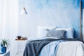 White lamp above table next to bed with blue and grey bedsheets