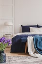 White lamp on stylish golden nightstand table next to king size bed with navy blue bedding