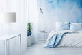 White lamp on a table in bright blue bedroom interior with bed a