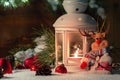 White lantern with a burning candle stands in the snow surrounded by Christmas decorations on the background of a wooden Royalty Free Stock Photo