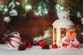 White lantern with a burning candle stands in the snow surrounded by Christmas decorations on the background of a wooden Royalty Free Stock Photo