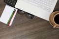 A white laptop, Notepad, pen, glasses, calculator, coffee mug ontable. Royalty Free Stock Photo