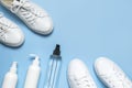 White leather sneakers, plastic bottles of cleaning products for shoes on blue background flat lay top view. Natural leather shoe