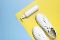 White leather sneakers, plastic bottles of cleaning products for shoes on blue yellow background flat lay top view. Natural