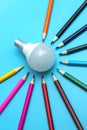 A white LED lamp surrounded by colored pencils on a blue background. The concept of one idea with a difference of opinion