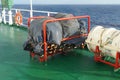 White life raft and embarkation ladder on deck of container ship ready to use in emergency situation.