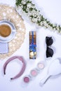 White lifestyle flat lay with coffee cup, candles, macarons cookies, white flowers, hairbrush and woman sunglasses.