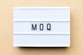 White lightbox with word MOQ Abbreviation of Minimum Order Quantity on wood background