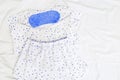 White Light pajama and blue eye mask on white sheet on bed. Night suit for peaceful sleeping