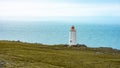 White lighthouse on a green cliff in front of the bright blue Atlantic Ocean on Iceland. Royalty Free Stock Photo