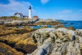 White lighthouse overlooking rocky coast in Maine with focus on rocks like petrified wood Royalty Free Stock Photo