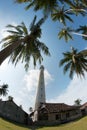 White lighthouse standing on an island surrounded by green palm trees.