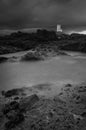 A white lighthouse standing on rocks with an incoming tide and a dark stormy sky.