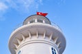 A white lighthouse stands against a blue sky. Over the lighthouse a red Turkish flag flies. Turkey, Alanya