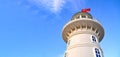 A white lighthouse stands against a blue sky. Over the lighthouse a red Turkish flag flies. Turkey, Alanya