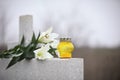 White lilies and candle on light grey tombstone outdoors. Funeral ceremony