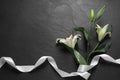 White lilies and ribbon on black table, flat lay with space for text. Funeral symbols