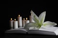 White lily, book and blurred burning candles on table in darkness, space for text. Funeral symbol Royalty Free Stock Photo
