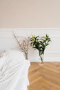 White lily flowers in a vase, tree branches in a vase near the bed. Details of the interior decor of the house