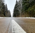 White line of road markings on asphalt, winter landscape on the road, trees in the forest, view of the road from below into the Royalty Free Stock Photo