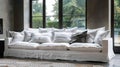A white linen sofa with multiple pillows sits in front of a large window with a view of a garden Royalty Free Stock Photo