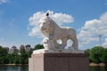 White lion sculpture, a dove sits on the lion`s head, against a blue sky with clouds, a river, trees and houses Royalty Free Stock Photo