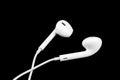 White little headphones isolated on black background. Earphones isolated on black background.