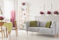 White living room interior with grey couch with cushions, rack with vases and books, fresh heathers, posters on wall